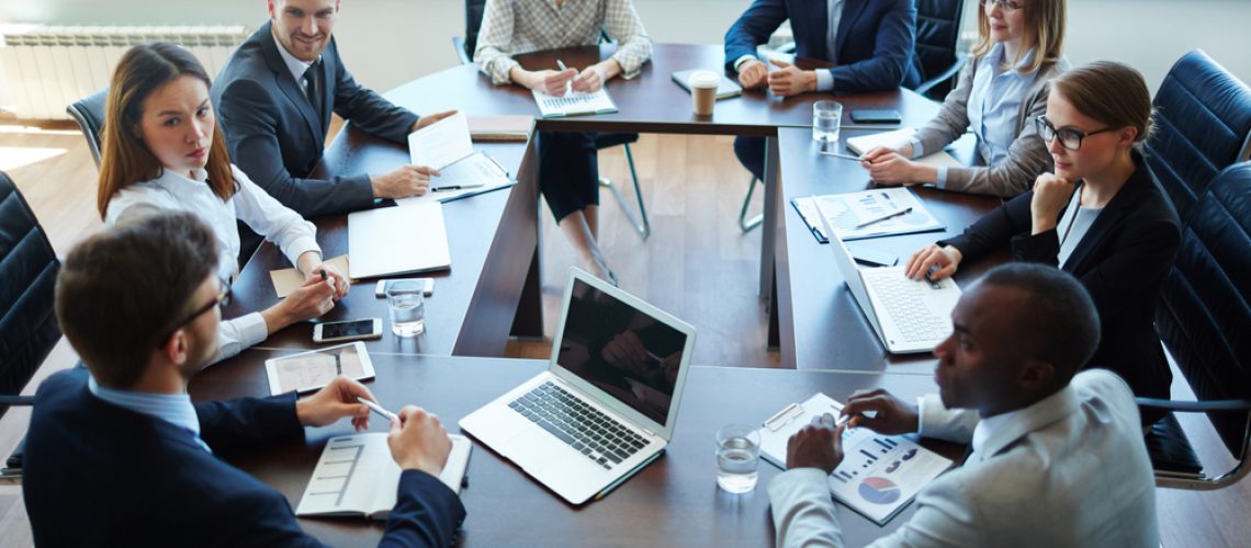 People gathered around a meeting table engaged in discussion, representing effective meeting processes on a high-performing team